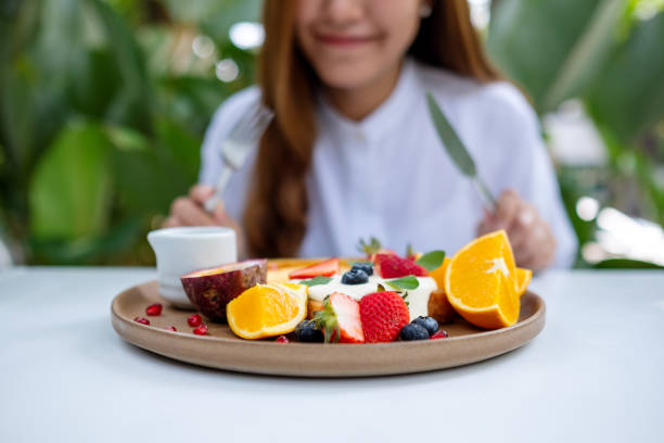 closeup of a young woman eating mixed fruits french toast brunch in restaurant - french toast breakfast food sweet food imagens e fotografias de stock