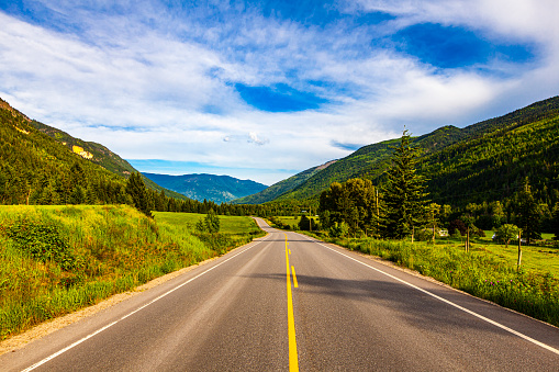 Road trip scene with sunlight and open road with blue sky, rich green mountains and valleys