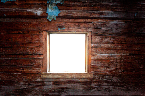 Old wooden cabin framed window with dark interior looking out into pure white background. Vintage, rustic wood theme.