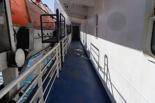 Exterior corridor of ship with railings and emergency lifeboats along long walkway