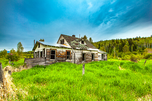 Old rustic wooden barn house or hunting cabin, overgrown grass and set against a stormy background