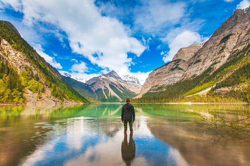 Young man looking out into a picturesque valley landscape reflected on a still mirrored lake