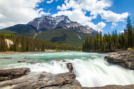 Snow capped rocky mountain landscape scene with powerful waterfall in foreground