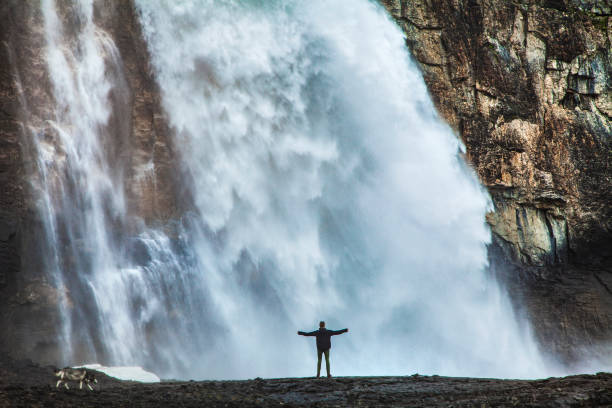 istock Young man standing with arms out beneath a large rushing waterfall 1398743827