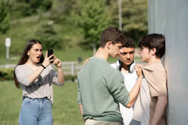 Two bullies menacing teenager boy and girl filming on phone. Cyber bullying and violence concept.