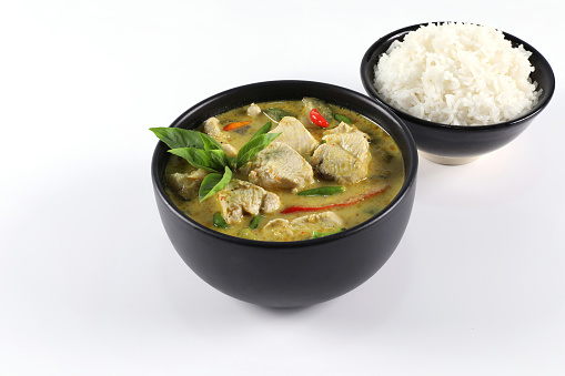 Thai food. Chicken green curry with rice in black bowl isolated on white background. Green curry with chicken consists of chicken breast, coconut milk, curry paste, basil, kaffir lime leaves, garden paprika.