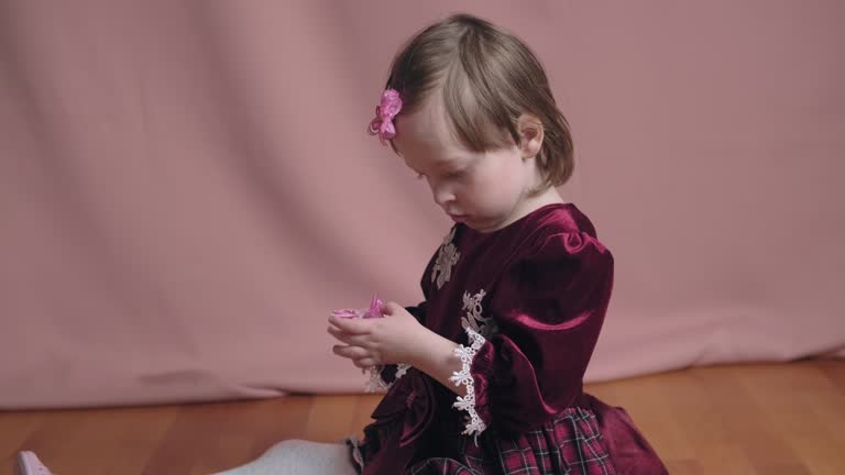 Cute little girl in an vintage burgundy dress is playing with a hair clip