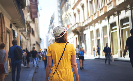 Woman tourist in red dress with hat walking on street of Rome on sunny day.