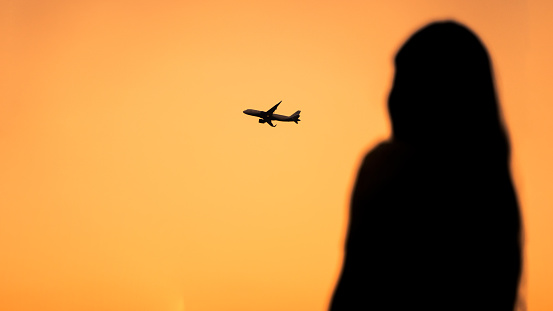 Silhouette of a female looking at an aeroplane during sunset or sunrise
