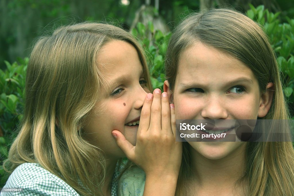 A little girl whispering into another girl's ear Two girls sharing a secret Child Stock Photo