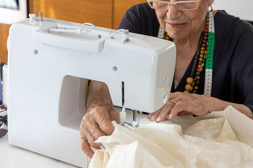 Well-groomed old woman using a sewing machine at home