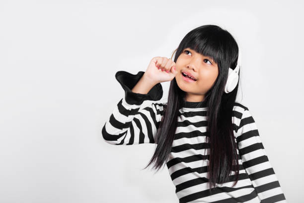 azjatyckie małe dziecko 10 lat uśmiecha się słuchając muzyki nosi bezprzewodowy zestaw słuchawkowy i trzyma rękę blisko ust śpiewa piosenkę - 8 9 years audio zdjęcia i obrazy z banku zdjęć