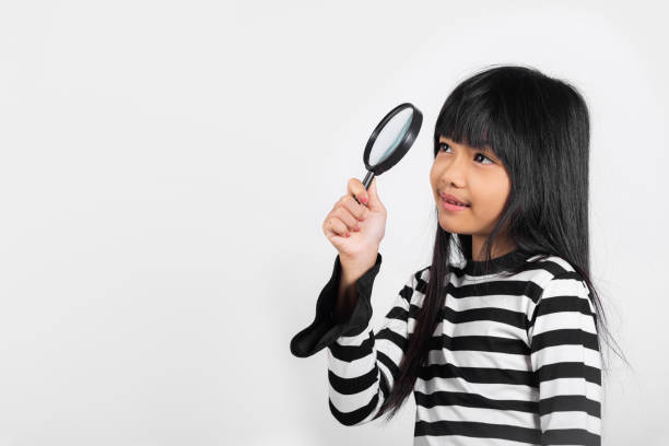 Asian little kid 10 years old funny looking through magnifying glass at studio shot isolated on white background, Happy child girl lifestyle smiling exploring holding magnifier searching