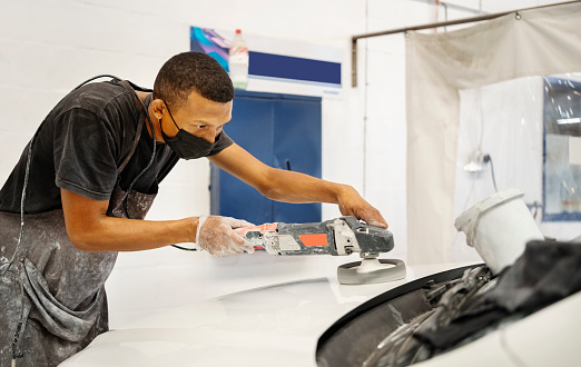 Technician polishing car hood using grinding machine after a primer coat at auto repair shop