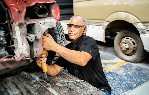 Senior man mechanical worker grinding the car chassis after welding in automobile garage