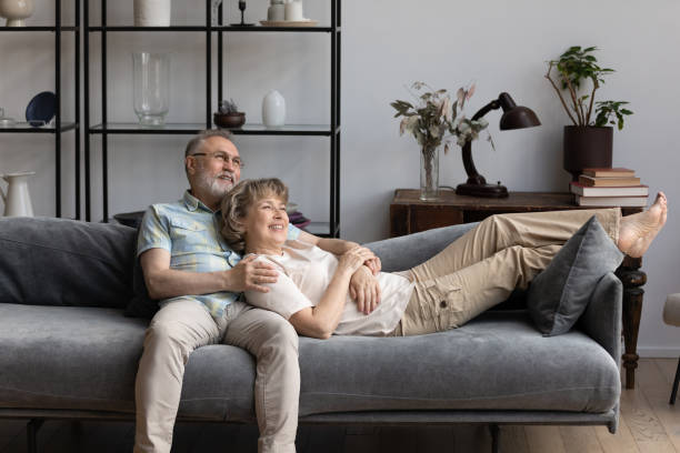 расслабленная счастливая пожилая пара отдыхает на уютном диване. - middle human age couple women стоковые фото и изображения