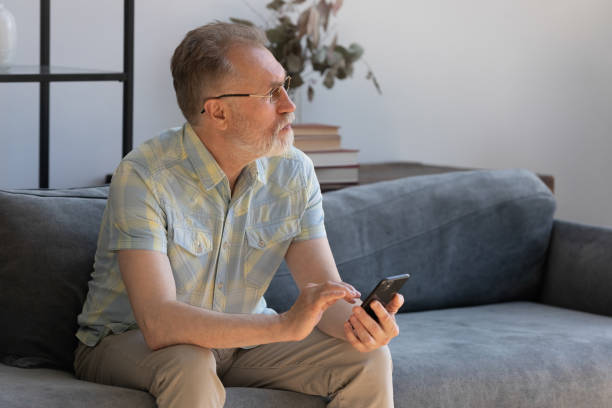 istock Dreamy old retired man using cellphone at home. 1398764350