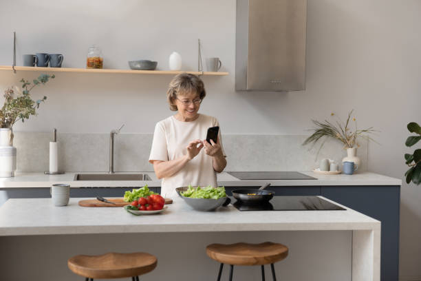 istock Happy middle aged old woman using cellphone preparing food. 1398764388