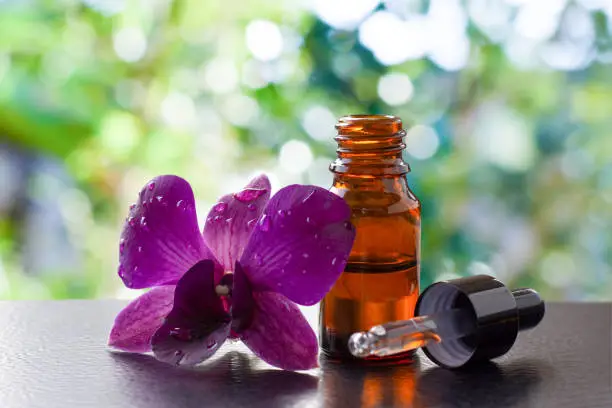 Bottle of essential oil with orchid flowers isolated on dark background.