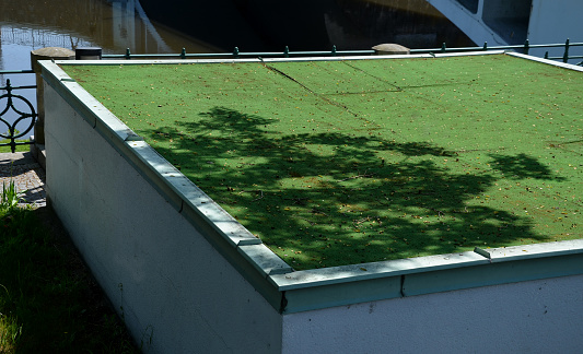 Plastic carpet on the roof of the building. The green beetle replaces the lawn which looks hako alive and real. flat-roofed buildings, garages, family houses by the river, artificial turf, outdoor