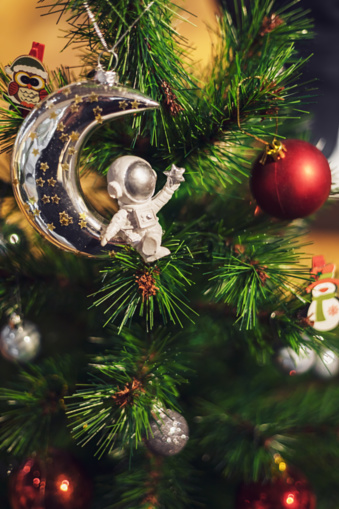 A silver figurine of astronaut and Christmas balls hang on a green spruce. Festive background. Defocused image