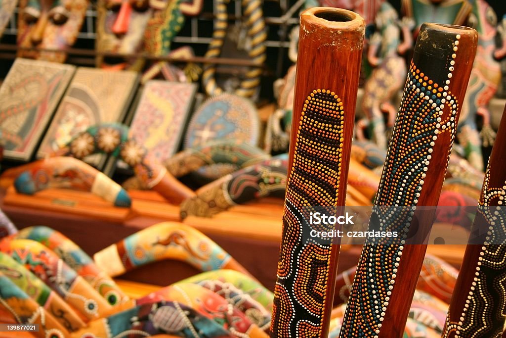 Australian crafts Didgeridoos on background of blurred aboriginal souvenirs, including boomerangs. Didgeridoo Stock Photo