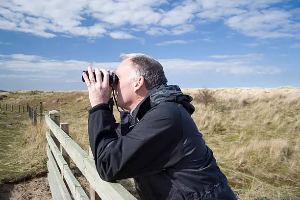 Middle aged white male observing wildlife through binoculars.
