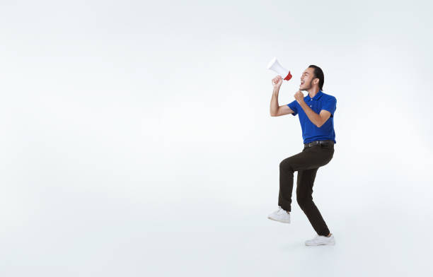 Asian delivery employee man shouting into megaphone making announcement isolated on white background. advertisement express delivery service concept. stock photo