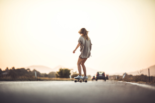 Back view of a woman skateboarding on the road in nature. Copy space.