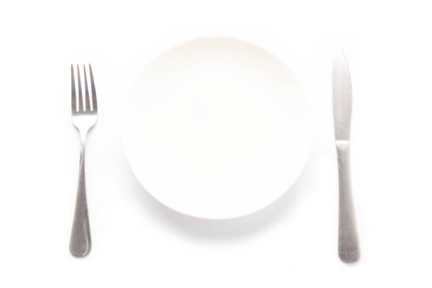 istock Empty white ceramic plate, knife and fork on a white table. For food, advertising space. 1398774400