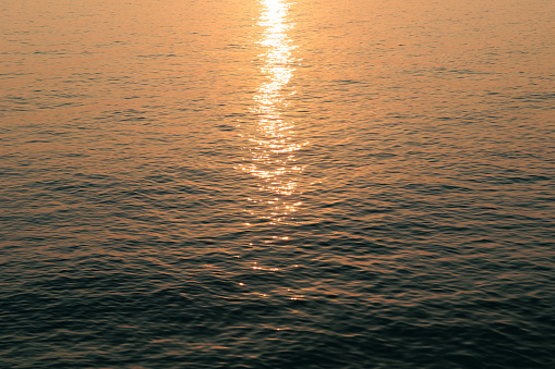 close up view of a marine water surface background illuminated in backlight by the sunlight at sunset, blue and orange color shades