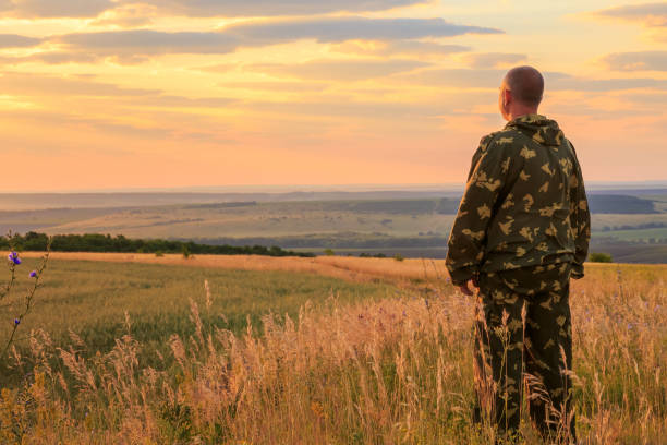 um agricultor europeu, de 40 a 45 anos, está em pleno crescimento em um campo no verão ao amanhecer no sol quente, tendo como pano de fundo o céu e o horizonte do pôr do sol. homem olhando para a distância - male 45 years old - fotografias e filmes do acervo