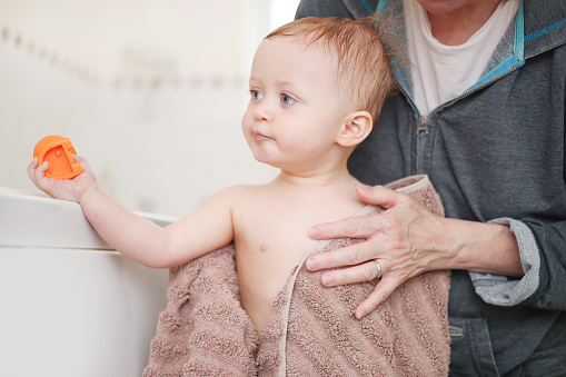 Cute 18 month old baby girl being dried off after her bath by her grandmother after her bath time.