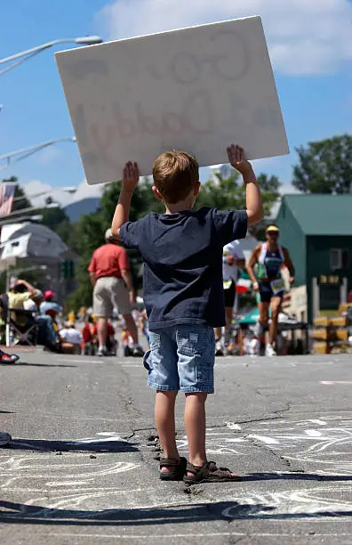Little boy cheering on daddy  by holding a sign during an ironman event.