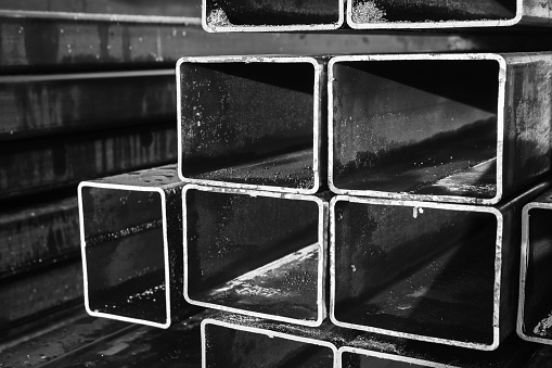 Black and white metallurgy background, stacked rolled metal products, steel pipes with rectangular cross-section