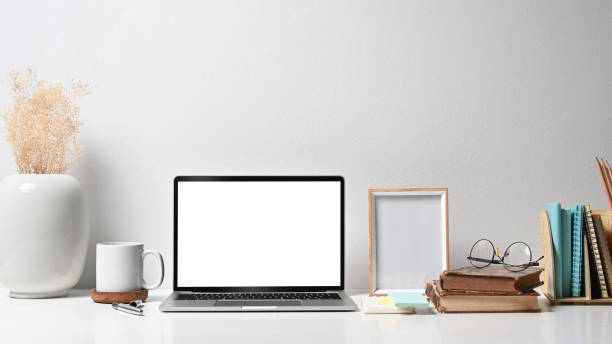 istock Comfortable workplace with laptop computer, picture frame, flower pot, coffee cup and stationery on white table. 1398780989