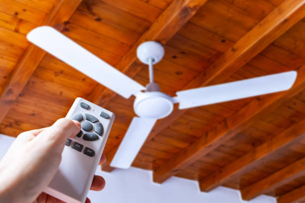 istock Close up shot of a hand using a remote control to operate a ceiling fan mounted in a house on a wooden ceiling. 1398782425