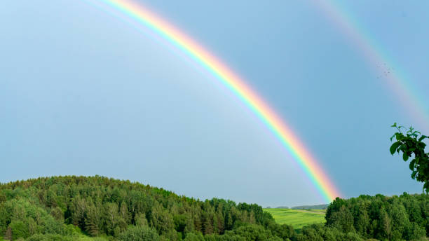 doppelter regenbogen an einem grauen himmel nach regen. ein seltenes atmosphärisches phänomen nach einem sturm. wunderschöne hügelige landschaft mit einem echten regenbogen nach regen an einem sommertag. - regenbogen stock-fotos und bilder