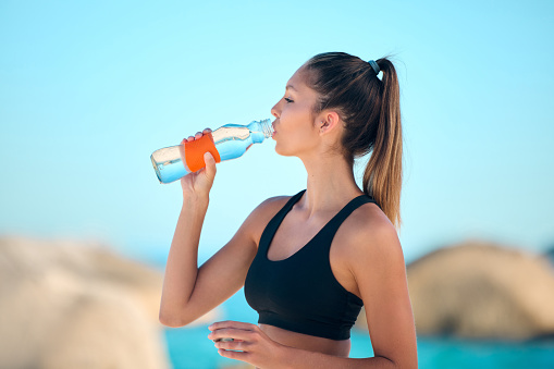 Beautiful woman practising yoga exercise on the beach. Young female athlete drinking water while working out outside. Taking a break. Finding inner peace and balance. Focused on a fitness lifestyle