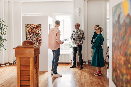 Gallery opening day, male gallery owner showing and explaining art to an interested group of visitors.