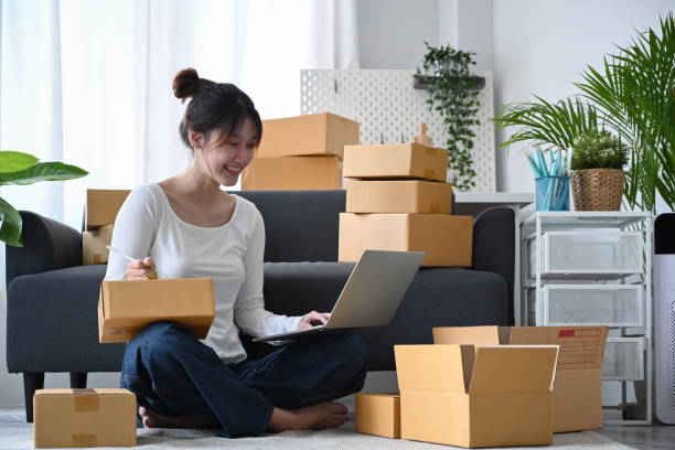 istock Young business woman answering customers through laptops and preparing parcel boxes of product for delivery. Online selling, e-commerce concept. 1398783081