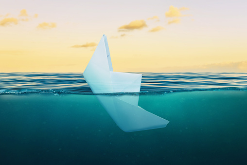 A paper ship sinking into the sea. The concept of failure in business and private life