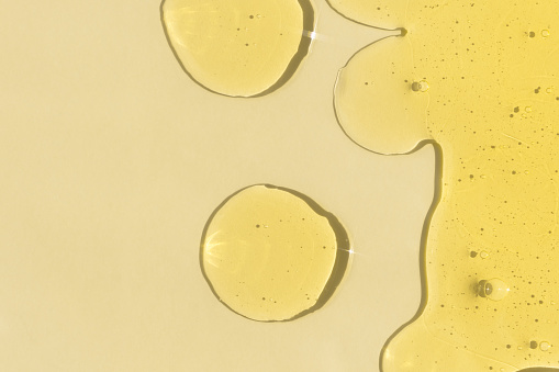 Drops of transparent cosmetic gel or serum yellow on a beige background. The concept of cosmetics or virus protection. Top view.