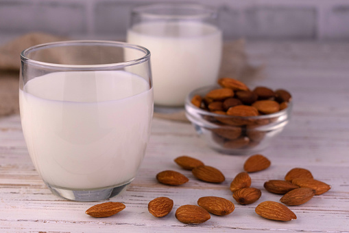 Two glasses of organic vegan almond milk on a white wooden background.