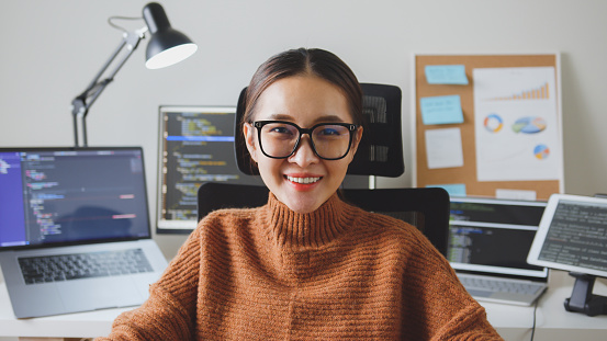 Portrait young Asian woman developer programmer, software engineer, IT support, wearing glasses look at camera and smile enjoy working at home.