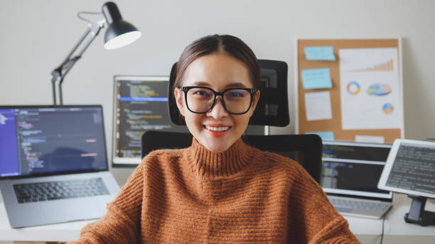 Portrait young Asian woman developer programmer, software engineer, IT support, wearing glasses look at camera and smile enjoy working at home. Portrait young Asian woman developer programmer, software engineer, IT support, wearing glasses look at camera and smile enjoy working at home. javascript stock pictures, royalty-free photos & images