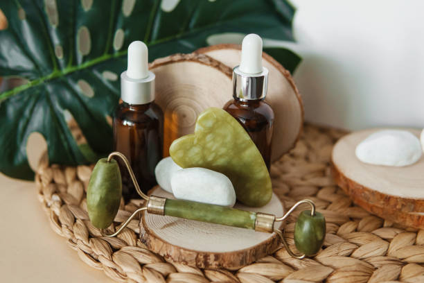 Jade Gua sha scraper and roller face massager, bottles of cosmetic serum for the face on wooden stands. stock photo