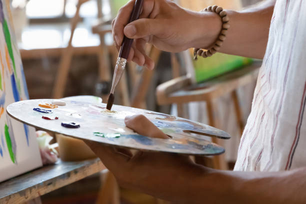 istock Artist hand holding palette at easel with oil, acrylic paints 1398786607