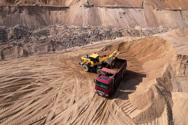Front end loader on earthworks in quarry. Wheel loader load sand in dump truck in open pit. Heavy machinery on developing opencast. Mining truck transports sand from open-pit mining, aerial view.