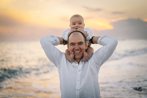 Happy Father's day. Father and baby play on the beach. Dad and him Child together enjoying sunset. Loving single father hugs cute little son.